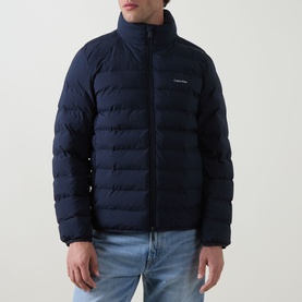 Model wearing Calvin Klein Logo Padded Jacket in Dark Sapphire, quilted funnel neck design with front zip, styled with blue jeans.