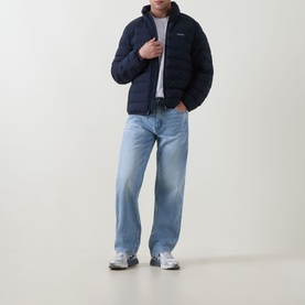 Model wearing Calvin Klein Logo Padded Jacket in Dark Sapphire, quilted funnel neck design, styled with light-wash jeans and white trainers.