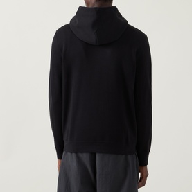 Model wearing Calvin Klein 350 Terry Stack Logo Hoodie in black, rear view, styled with dark grey trousers.