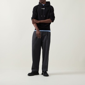 Model wearing Calvin Klein 350 Terry Stack Logo Hoodie in black with grey wide-leg trousers and black loafers.