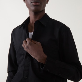 Model wearing black long-sleeve shirt, open collar, layered over white crew-neck tee