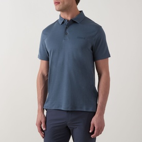 Model wearing Calvin Klein Badge Logo Polo Shirt in Dark Slate, short sleeves, three-button placket, tonal chest logo, styled with grey trousers.