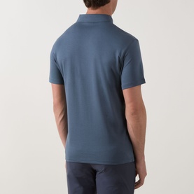 Model wearing Calvin Klein Badge Logo Polo Shirt in Dark Slate, back view showing short sleeves and straight hem, styled with navy trousers.
