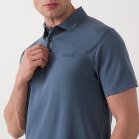 Model wearing Calvin Klein Badge Logo Polo Shirt in Dark Slate, showing tonal chest badge, three-button placket and short sleeves.