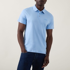 Model wearing Calvin Klein Badge Logo Polo Shirt in Placid Blue, with polo collar, three-button placket and tonal chest logo, styled with dark jeans.