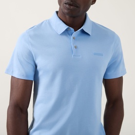 Model wearing Calvin Klein Badge Logo Polo Shirt in Placid Blue, featuring polo collar, three-button placket and tonal chest logo badge.