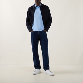 Model wearing Calvin Klein Badge Logo Polo Shirt in Placid Blue, styled with a dark navy jacket, navy trousers and white trainers.