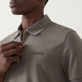 Model wearing Calvin Klein Supima Slim Zip Polo Shirt in Bungee Cord, showing half-zip placket, polo collar and tonal logo badge detail.