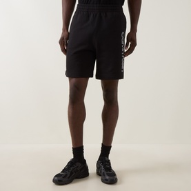 Model wearing Calvin Klein black cotton shorts with logo print on left leg, styled with black chunky trainers