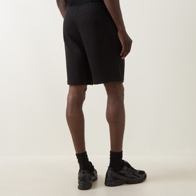 Model wearing Calvin Klein black cotton sweat shorts, rear view, styled with black socks and dark chunky trainers.