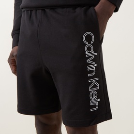 Model wearing Calvin Klein black cotton shorts with large vertical logo print on left leg, paired with black long-sleeve top.