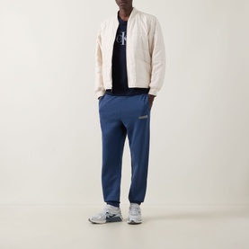 Model wearing Calvin Klein 350 Logo Sweatpants in Dark Denim, cuffed terry joggers with logo badge, styled with cream bomber jacket.
