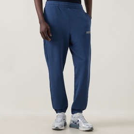 Model wearing Calvin Klein 350 Logo Sweatpants in Dark Denim, cuffed terry cotton joggers with elasticated waist, styled with silver trainers.