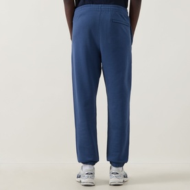 Model wearing Calvin Klein 350 Logo Sweatpants in Dark Denim, cuffed ankle style, elasticated waist, paired with white trainers.