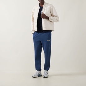 Model wearing Calvin Klein 350 Logo Sweatpants in Dark Denim, cuffed terry joggers with logo badge, styled with cream zip jacket.