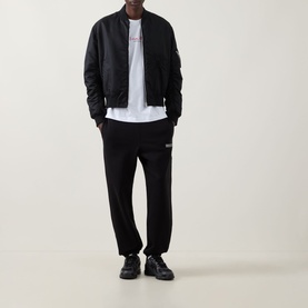 Model wearing Calvin Klein 350 Logo Sweatpants in black with matching bomber jacket, white tee, and black trainers.