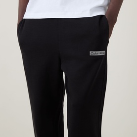 Model wearing Calvin Klein 350 Logo Sweatpants in black, showing rear logo badge detail, elasticated waistband, styled with white T-shirt.