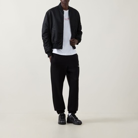 Model wearing Calvin Klein 350 Logo Sweatpants in black with cuffed hems and logo badge, styled with black bomber jacket and white tee.