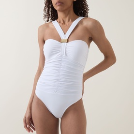 Model wearing white ruched halterneck swimsuit with gold ring detail at centre front neckline