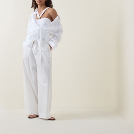 Model wearing white off-shoulder oversized shirt with matching wide-leg trousers, styled with brown flat sandals and layered necklace