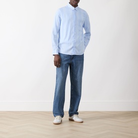 Model wearing Samsoe & Samsoe Ryan Stripe Shirt in Windsurfer St., light blue stripes, long sleeves, styled with mid-wash jeans and white trainers