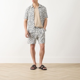 Model wearing Samsoe & Samsoe Salute Symmetry shorts with matching printed short-sleeve shirt and brown slide sandals.