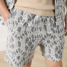 Model wearing Samsoe & Samsoe Salute Symmetry shorts in grey and cream jacquard pattern, hands in pockets, styled with a beige knit top.