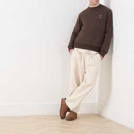 Model wearing Samsoe & Samsoe Joel Logo Sweatshirt in Turkish Coffee with crew neck, styled with cream wide-leg trousers and brown suede shoes.