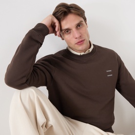 Model wearing Samsoe & Samsoe Joel Logo Sweatshirt in Turkish Coffee, crew neck with small logo detail, styled with cream trousers and collared shirt
