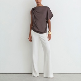 Model wearing Reiss purple drape-shoulder top styled with white wide-leg trousers and gold cuff bracelet