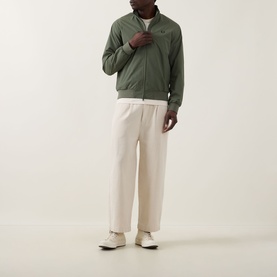 Model wearing Fred Perry Brentham Logo Overshirt in Laurel Wreath Green with zip fastening, styled with cream wide-leg trousers and white trainers.