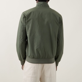 Model wearing Fred Perry Brentham Logo Overshirt in Laurel Wreath Green, back view, ribbed hem and cuffs, styled with cream trousers.