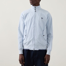 Model wearing Fred Perry Dusky Blue casual jacket with zip front, stand collar, and embroidered logo, styled with navy trousers.