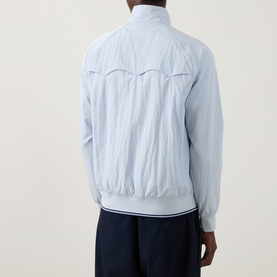 Model wearing Fred Perry Dusky Blue casual jacket, back view, with navy trousers. Lightweight fabric with ribbed cuffs and hem.