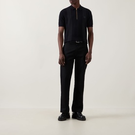 Model wearing Fred Perry Panel Detail Knitted Polo Shirt in black with half-zip placket, styled with black trousers and loafers.