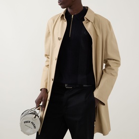 Model wearing Fred Perry Panel Detail Knitted Polo Shirt in Black with half-zip placket, styled with a beige coat and black trousers, carrying a