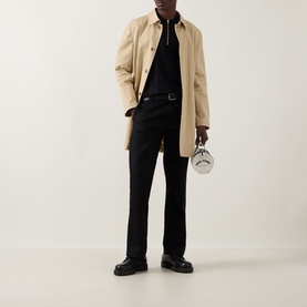 Model wearing Fred Perry Panel Detail Knitted Polo Shirt in Black, styled with a beige mac coat, black trousers, and chunky black loafers.
