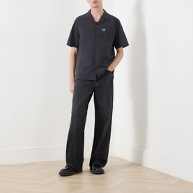 Model wearing Fred Perry Anchor Grey casual shirt with camp collar and short sleeves, styled with wide-leg dark trousers and black shoes.