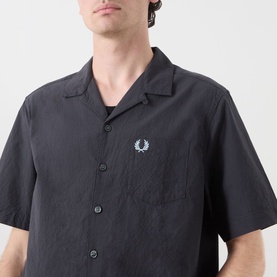 Model wearing Fred Perry Anchor Grey casual shirt with camp collar, short sleeves, and embroidered laurel wreath logo on chest pocket.