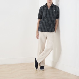 Model wearing Fred Perry navy striped cotton casual shirt with short sleeves, styled with cream wide-leg trousers and black slip-on shoes.
