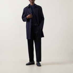 Model wearing Fred Perry Geometric Print Laurel Logo Polo Shirt in Twilight Navy, styled with a navy overcoat, black trousers and dark loafers.
