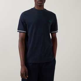 Model wearing Fred Perry navy crew neck T-shirt with green laurel wreath logo and chequerboard trim detailing at sleeves.