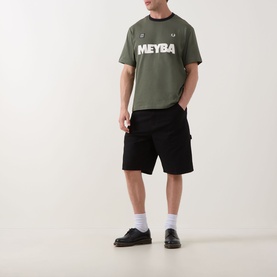 Model wearing Fred Perry Meyba Ringer T-Shirt in Laurel Wreath Green with black shorts and black shoes.