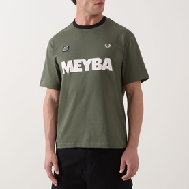 Model wearing Fred Perry Meyba Ringer T-Shirt in Laurel Wreath Green with black contrast ringer neckline and bold MEYBA graphic print.