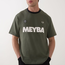 Model wearing Fred Perry Meyba Ringer T-Shirt in Laurel Wreath Green with navy ringer collar and bold MEYBA graphic print to chest.