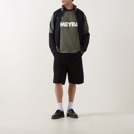 Model wearing Fred Perry Meyba Ringer T-Shirt in Laurel Wreath Green with black shorts, jacket, and loafers