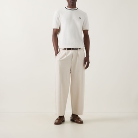 Model wearing Fred Perry Ecru Crew Neck T-Shirt with tipping detail, styled with cream wide-leg trousers, brown belt and loafers.