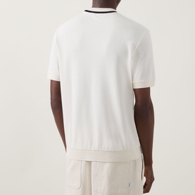 Model wearing Fred Perry Ecru Cotton Crew Neck T-shirt, rear view, with black tipping detail at collar and cuffs, styled with cream shorts.