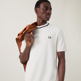 Model wearing Fred Perry Crew Neck T in Ecru with tipped collar detail, paired with a rust orange jacket draped over shoulder.