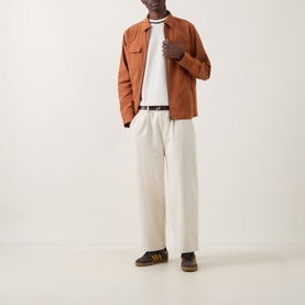 Model wearing Fred Perry Ecru Crew Neck T-Shirt, styled with tan overshirt, cream trousers, and dark suede trainers.
